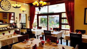 A restaurant with multiple tables, red curtains, and a clock on the wall.