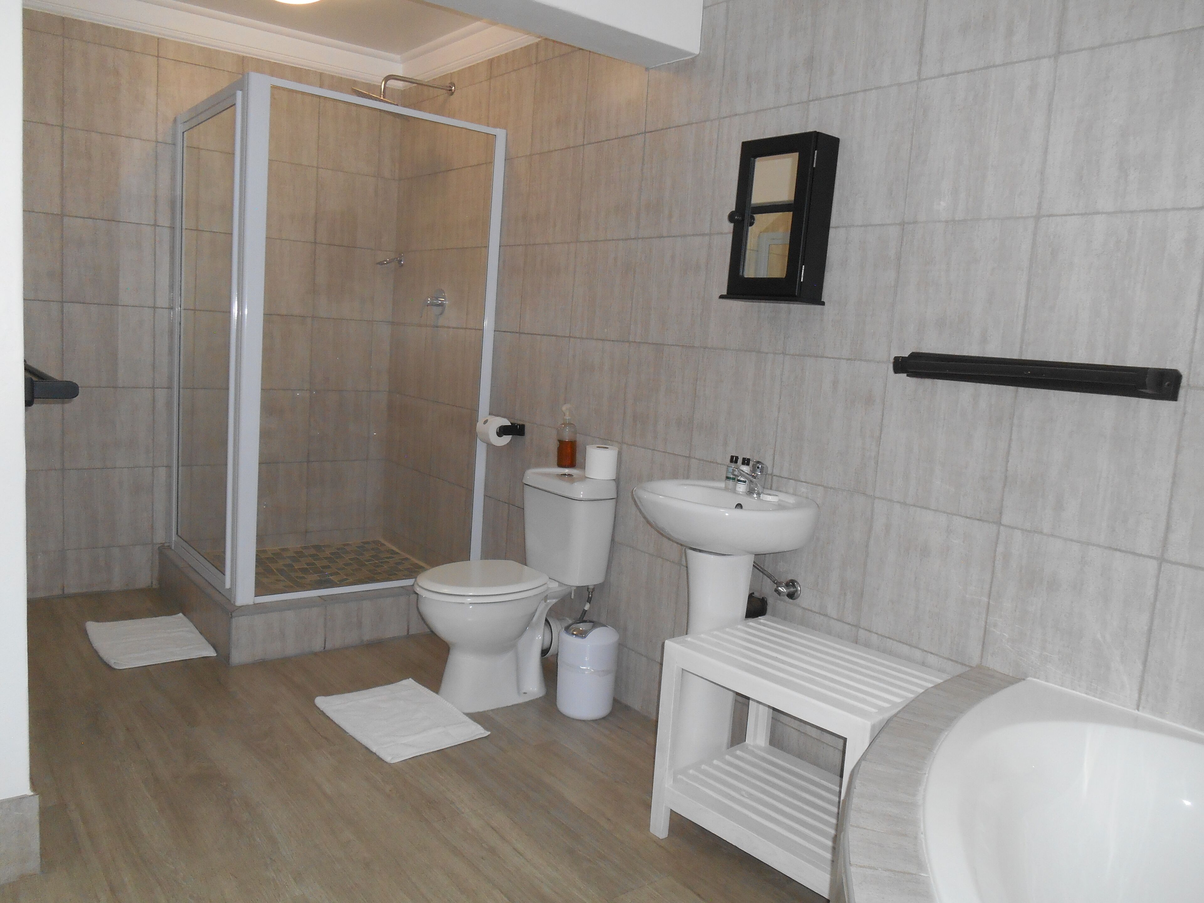 A bathroom with a shower, toilet, sink, and a small white stool.