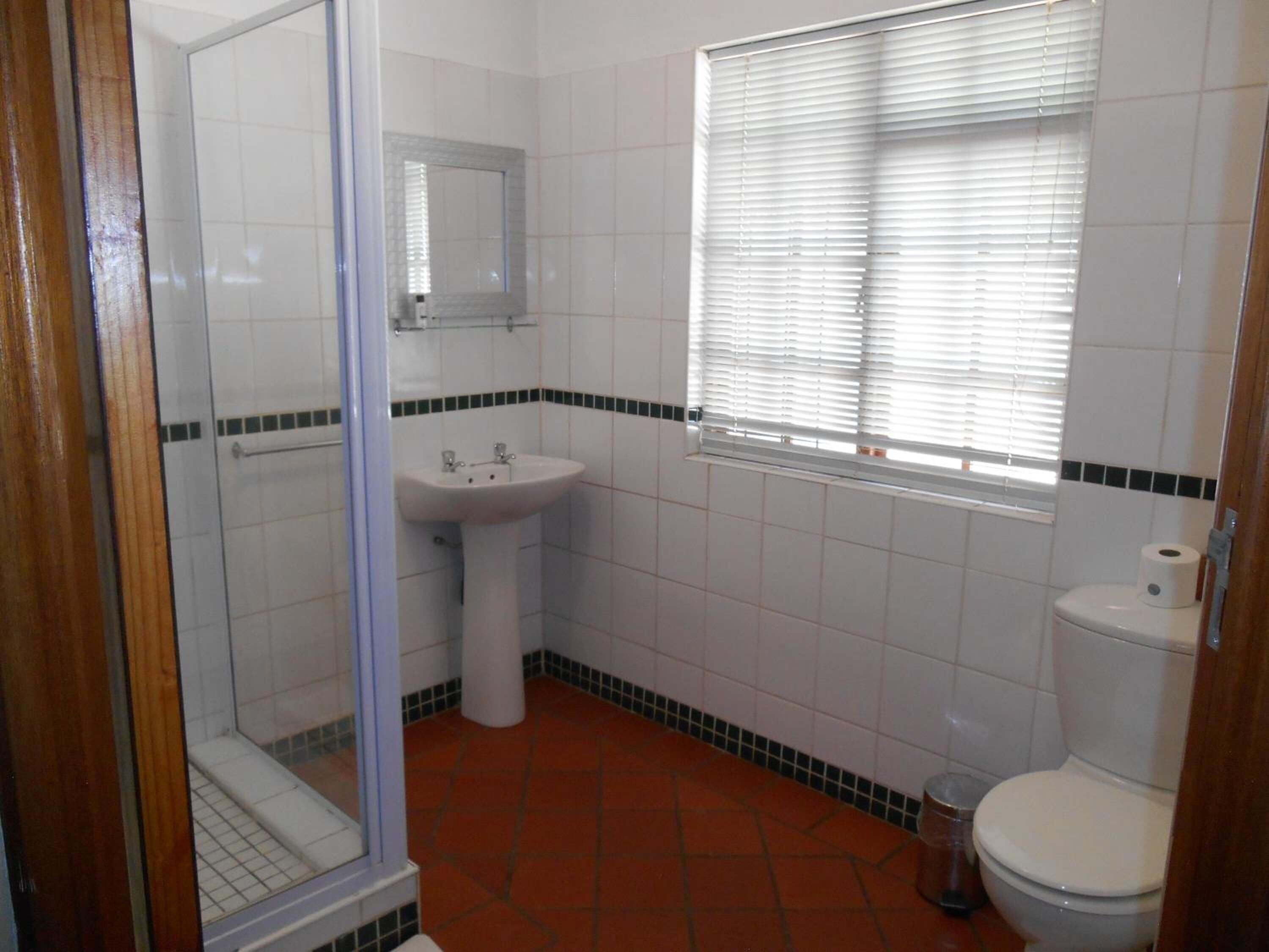 A bathroom with a shower, sink, toilet, and a window with blinds.