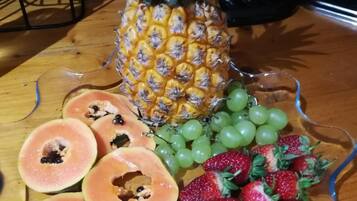 Une assiette de fruits comprenant de l’ananas, des raisins, des fraises, des kiwis et des papayes, posée sur une table en verre.