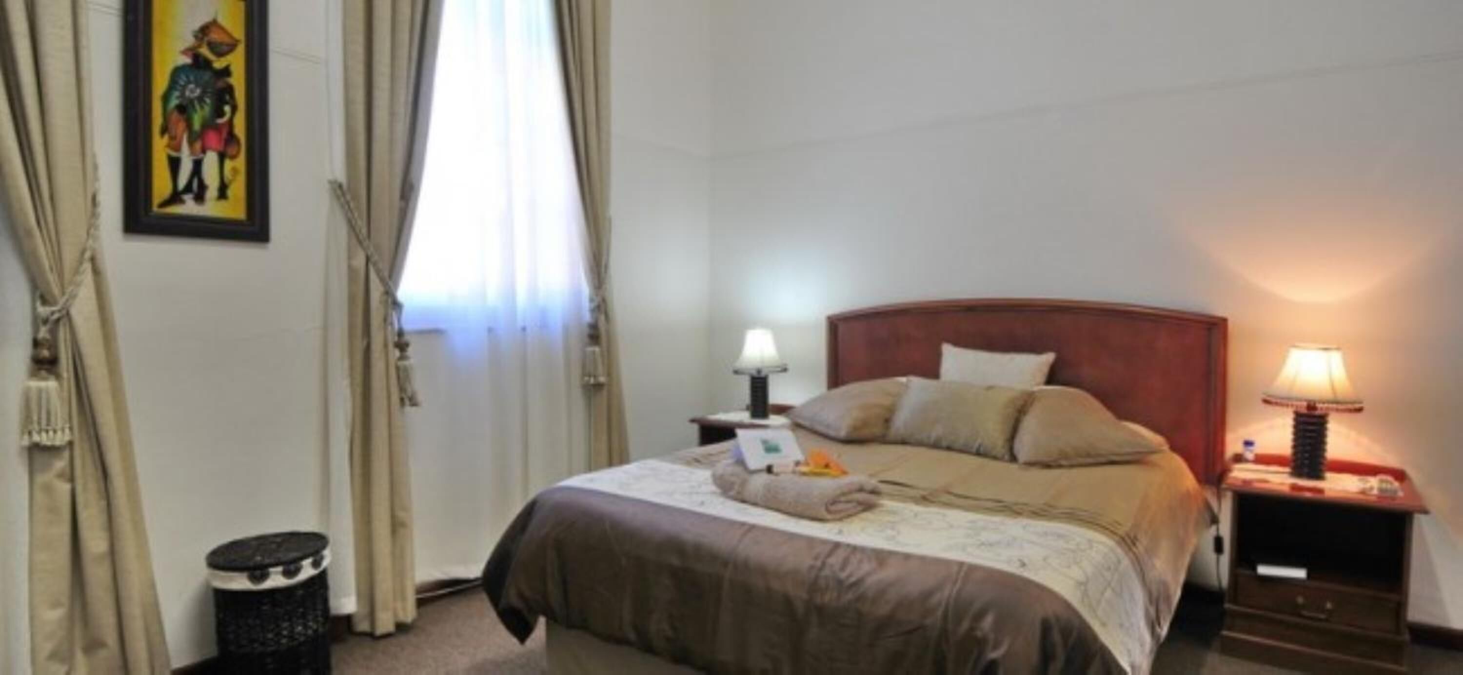 Hotelkamer met een bed, twee nachtkastjes, een lamp, een prullenbak en een schilderij aan de muur.