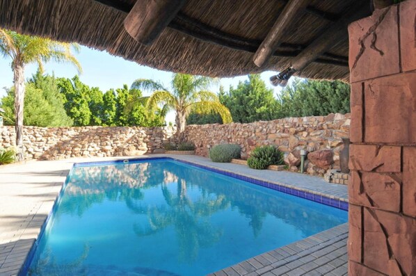 Une piscine avec un mur en pierre et une structure surmontée d’un toit de chaume.