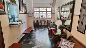 A reception area with a counter, seating, and a window with lace curtains. - Oasis Country Lodge (Matzikama)