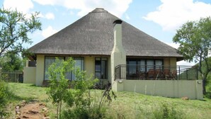 A thatched-roof house with a paved pathway leading to it, surrounded by greenery. - Leselo La Bontshi Lodge (Groblersdal)