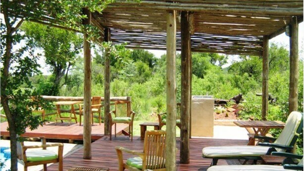 An outdoor wooden deck with seating, including chairs and a table, surrounded by lush greenery. - Leselo La Bontshi Lodge (Groblersdal)