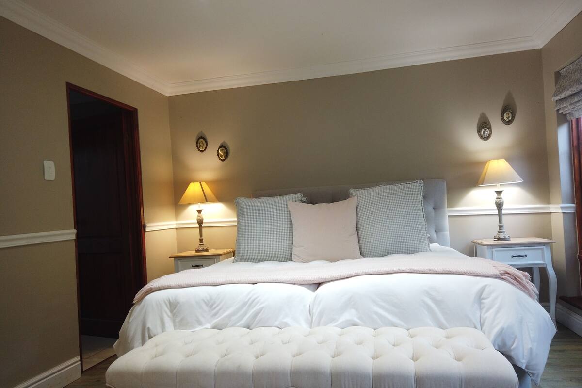 A bedroom with a large bed, two bedside tables with lamps, a door, and wall decorations.