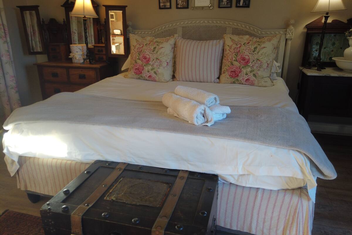 A neatly made bed with rolled towels, a vintage trunk, and a bedside lamp.