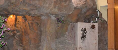 Una pared de roca con una escultura de metal de una rana y un pequeño estanque con una zona protegida por una red.