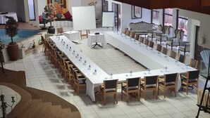 Een vergaderzaal met een lange tafel, stoelen en een podium met achtergrond.