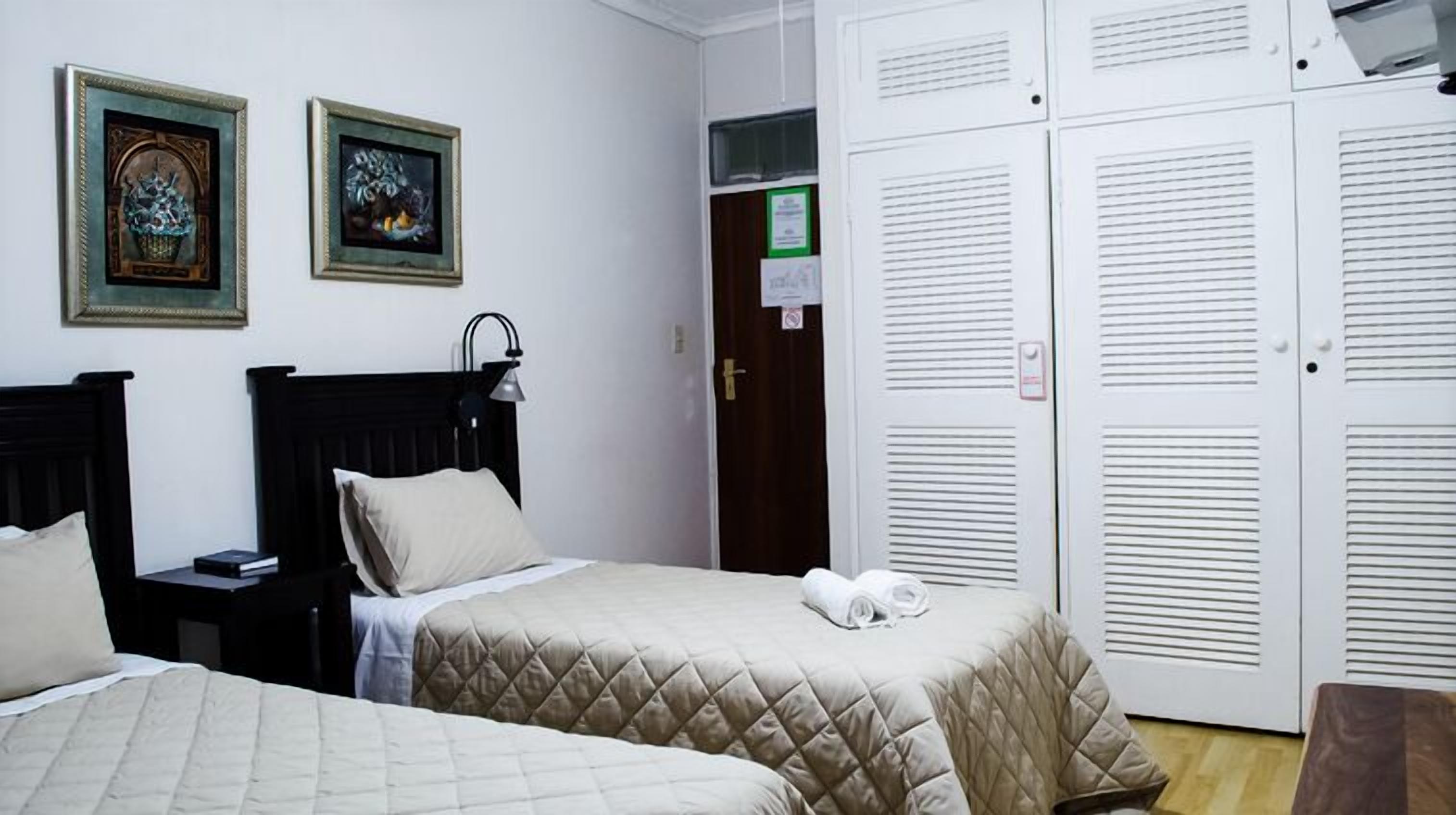 A hotel room with two beds, a nightstand, a lamp, and a wardrobe.