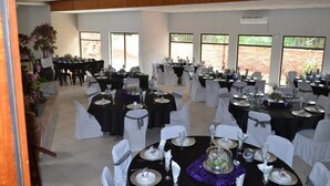 Een balzaal met meerdere ronde tafels, gedekt voor een formeel evenement, met witte stoelen en zwarte tafellakens.