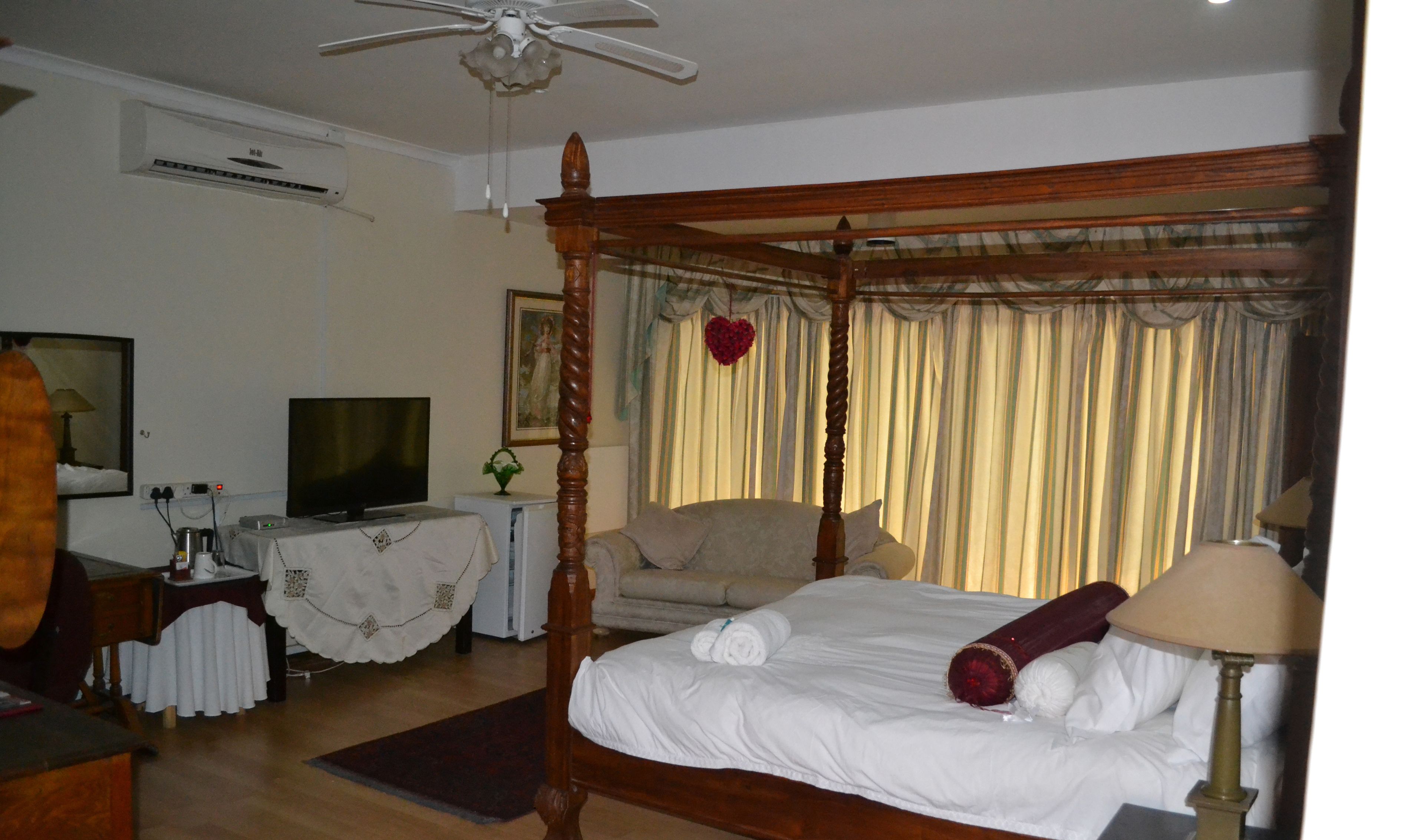 Ein Schlafzimmer mit Himmelbett, Fernseher, Schreibtisch mit Lampe und einem fensterbelaubten Fenster.