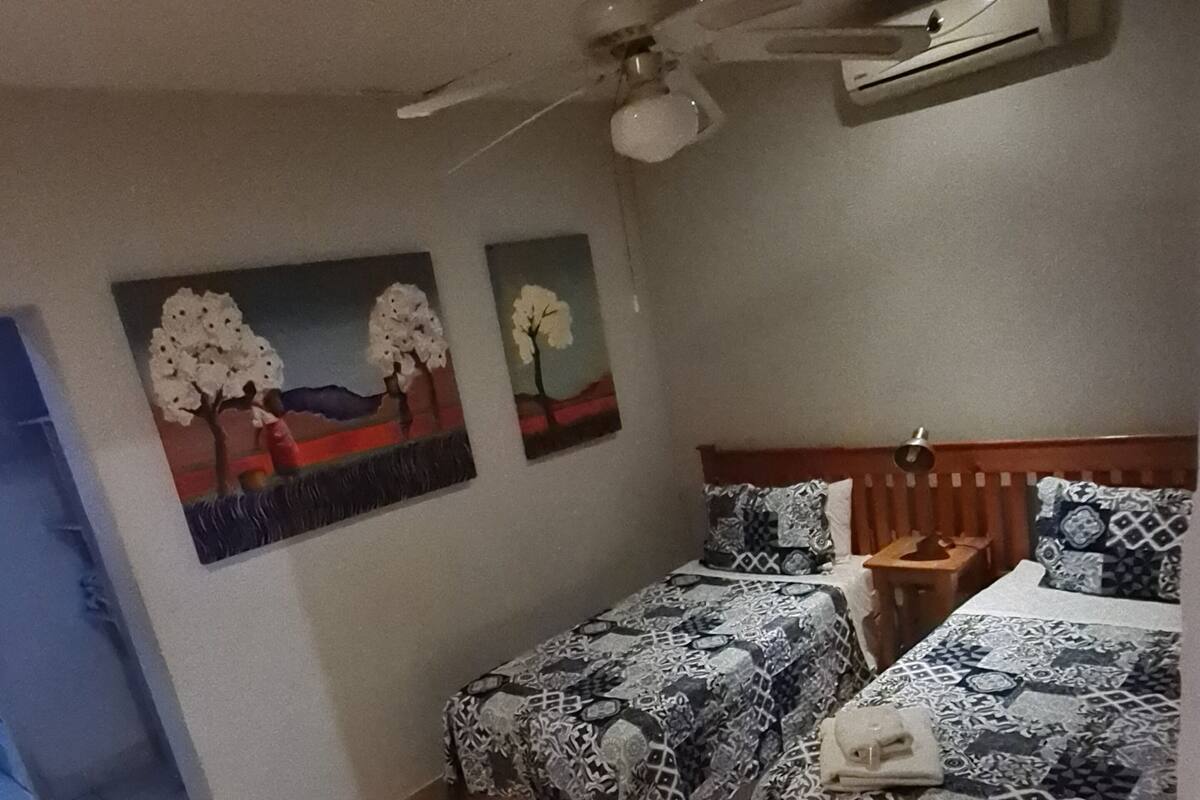 Un dormitorio con dos camas, una mesa de madera y un ventilador de techo.