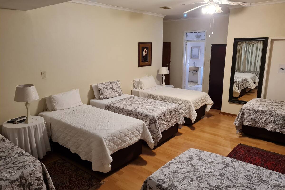 Habitación de hotel con tres camas, una mesita con una lámpara, un espejo y una puerta que da al baño.