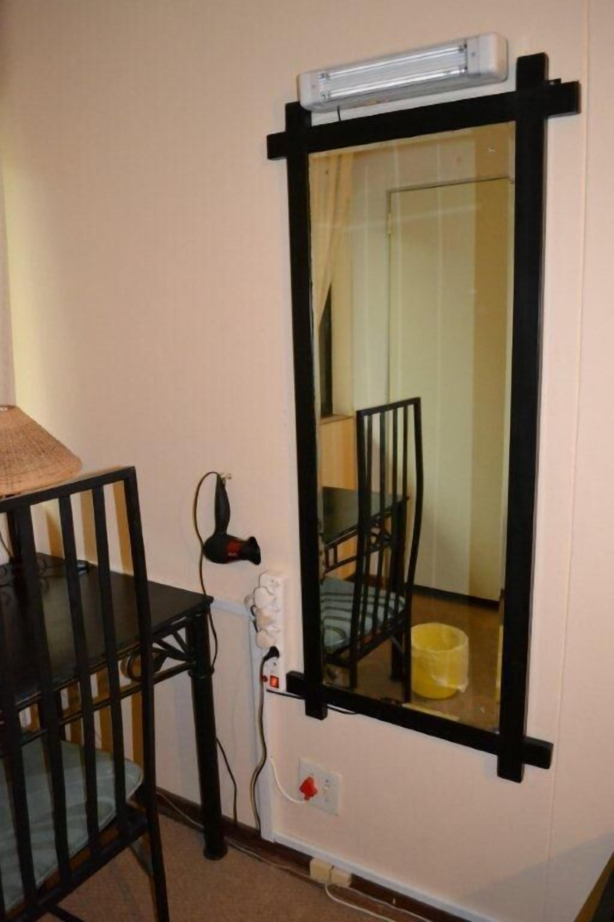 Una habitación con un espejo de marco negro, una mesa negra con una silla y una lámpara.