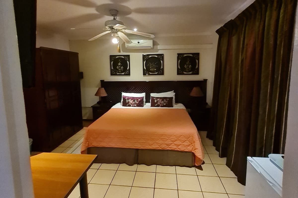 Habitación de hotel con cama, ventilador de techo, calefacción y ventana con cortinas.