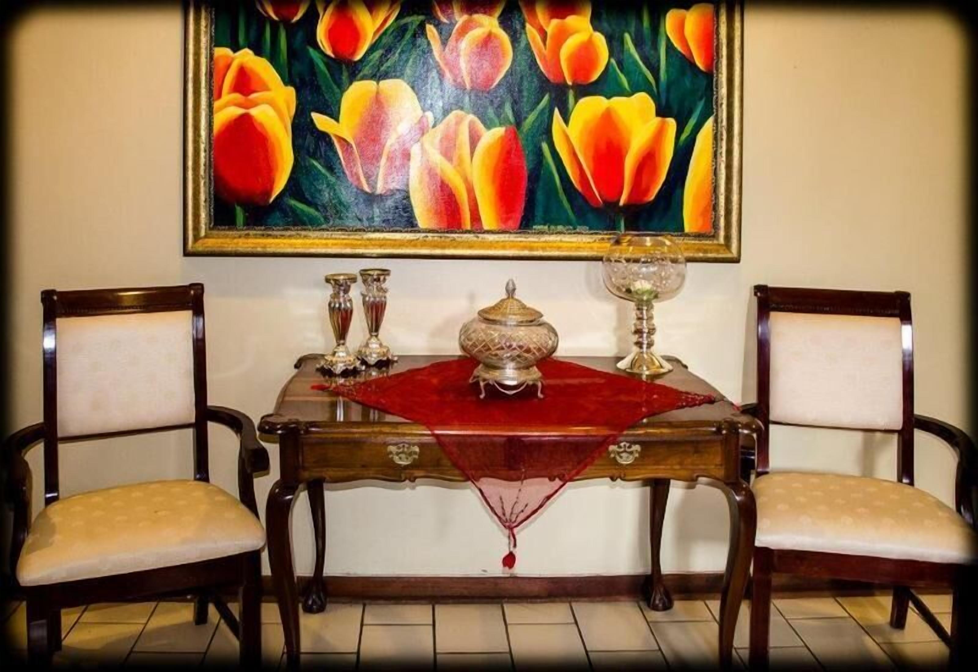 A dining table with two chairs, a painting of tulips, and a decorative centerpiece.
