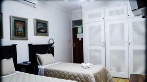 Een hotelkamer met twee bedden, een garderobe en kunstwerken in lijsten aan de muur.