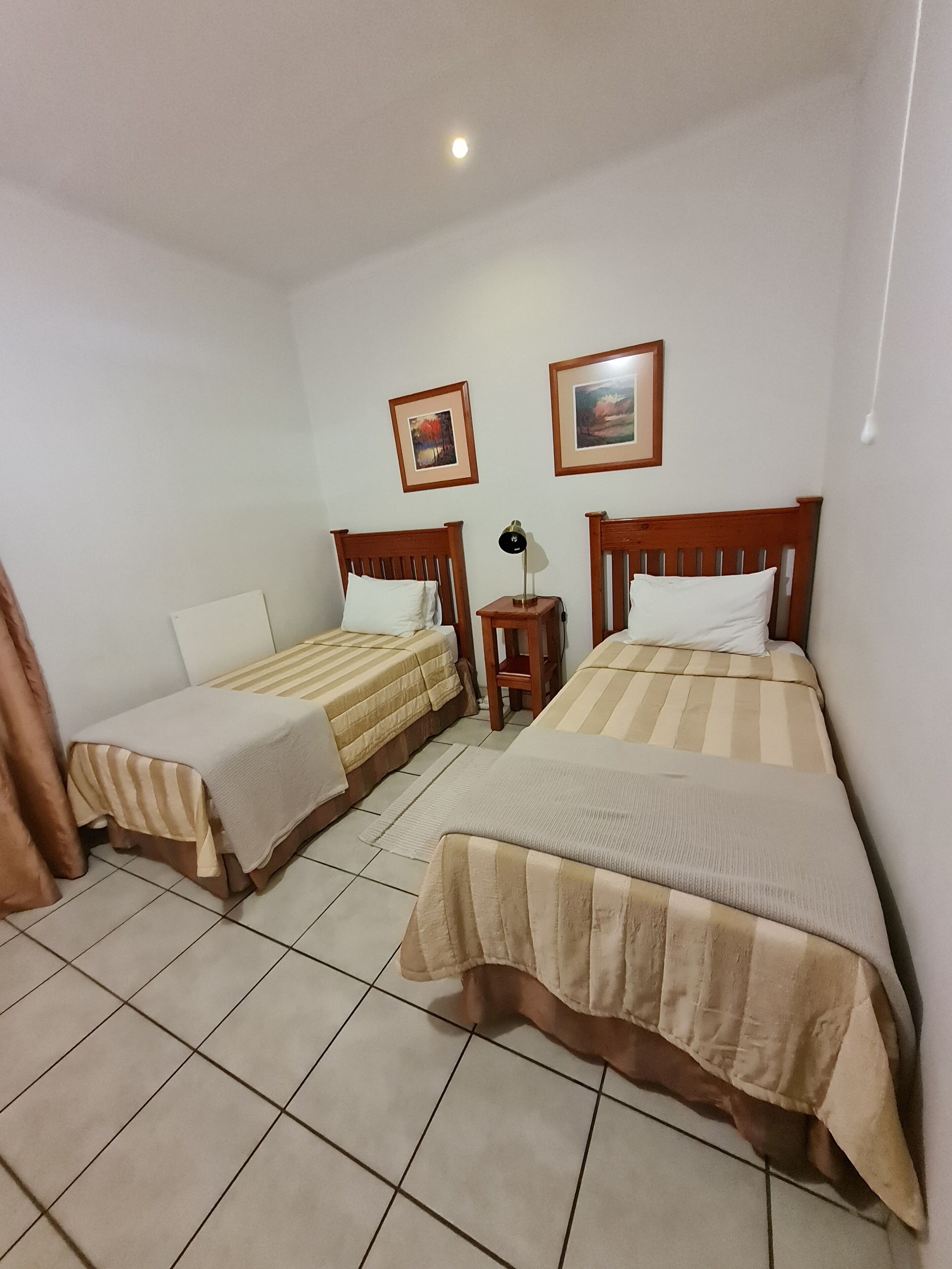 A room with two single beds, a nightstand with a lamp, and two framed pictures on the wall.
