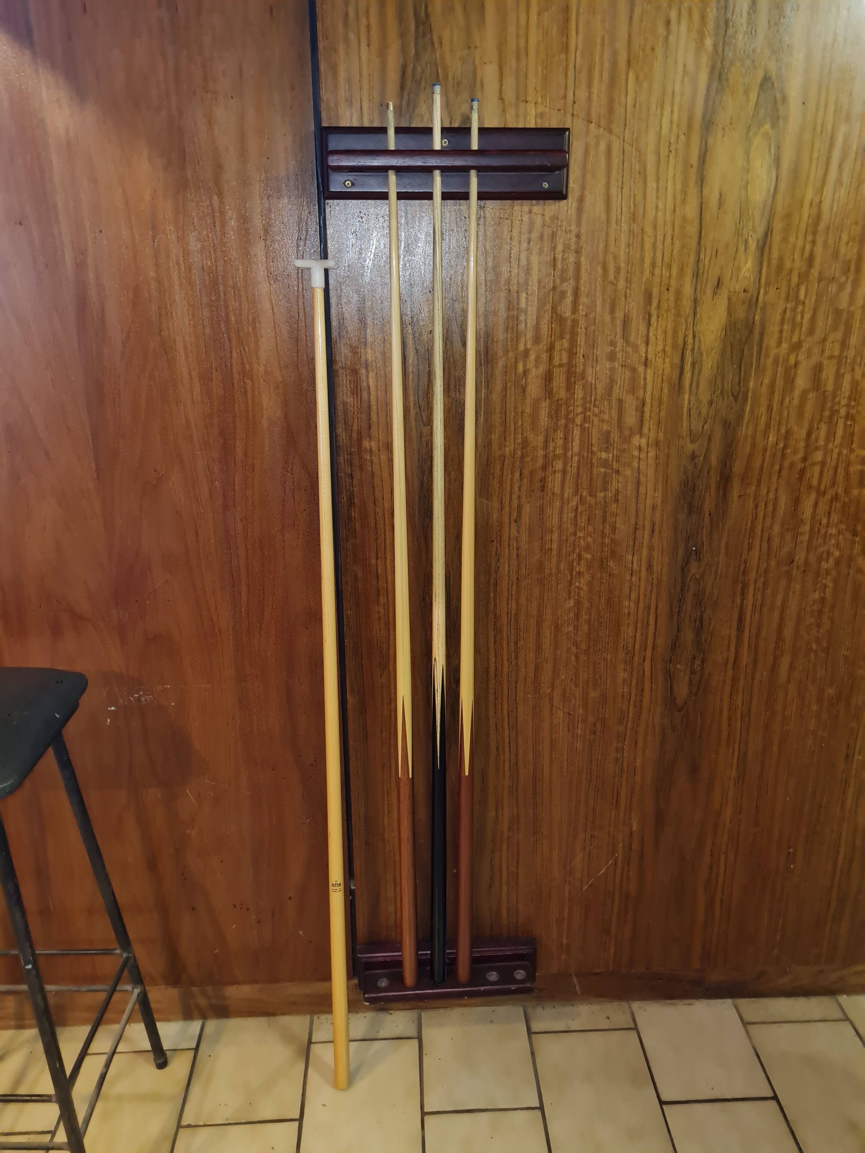 A wooden wall with a rack holding several pool cues.