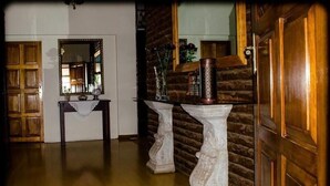 Een gang met een houten deur, een spiegel, een kleine tafel met een vaas en een decoratief voetstuk.