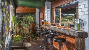 A bar area with wooden bar stools, a tiled backsplash, and a view of the outdoors. - Dungbeetle River Lodge (Colchester)