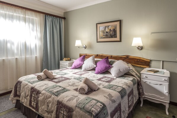 A neatly made bed with a quilt, pillows, and rolled towels. There are two bedside tables with lamps and a framed picture on the wall. - Dungbeetle River Lodge (Colchester)