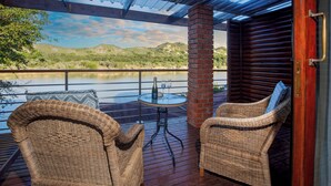 A covered outdoor area with wicker furniture and a table, overlooking a river and hills. - Dungbeetle River Lodge (Colchester)