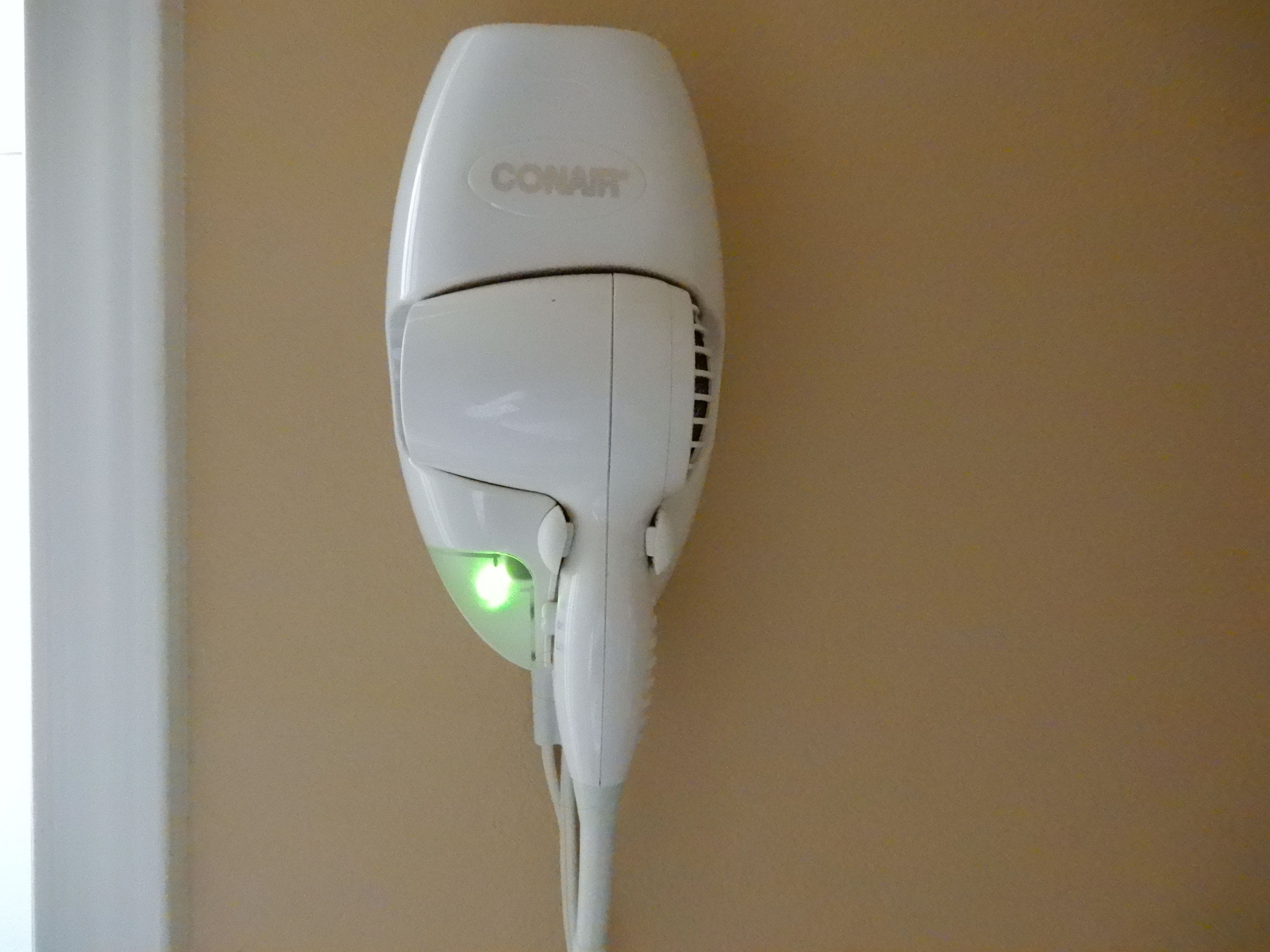 A white Conair hair dryer mounted on a beige wall.