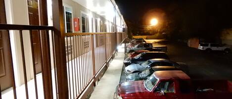 A parking lot with several cars parked in a row, a red truck, and a building with a balcony in the background.