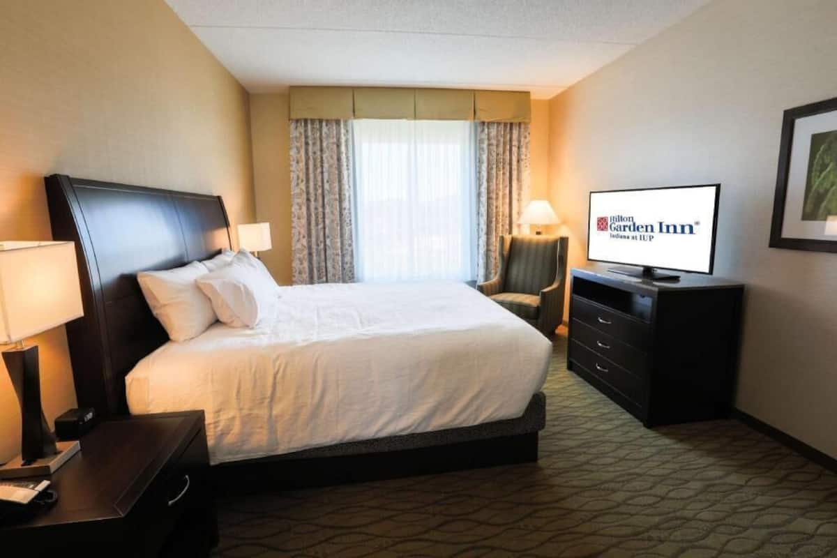 A hotel room with a bed, a TV, a desk, and a chair.