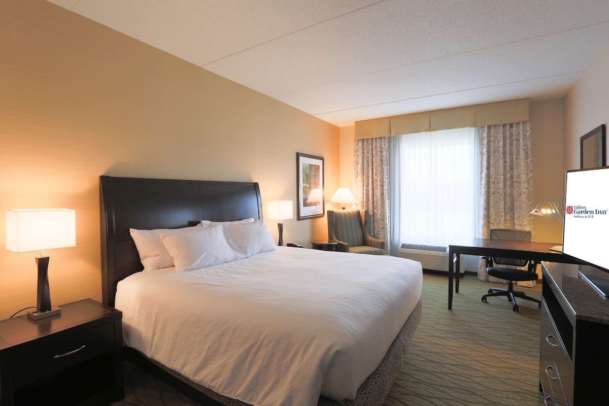 A hotel room with a large bed, a desk with a chair, a TV, and a window with curtains.