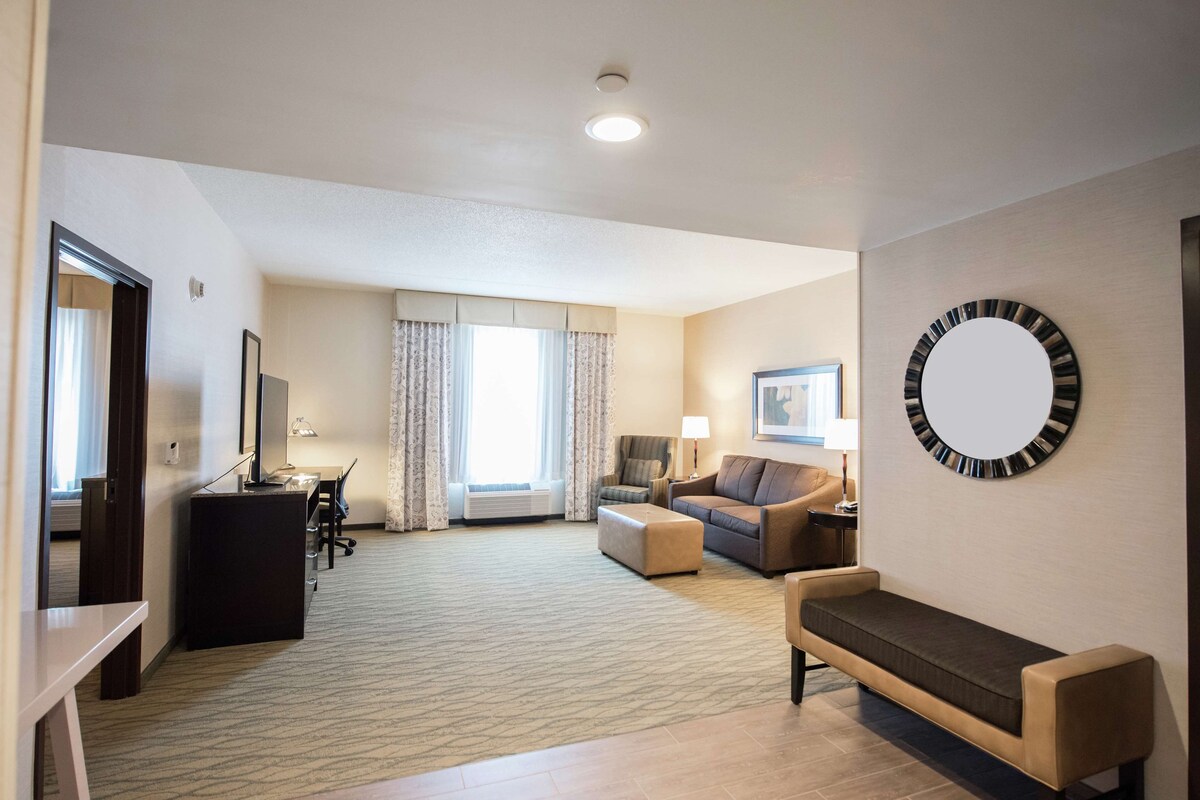 A hotel room with a desk, two sofas, a large mirror, and a window with curtains.