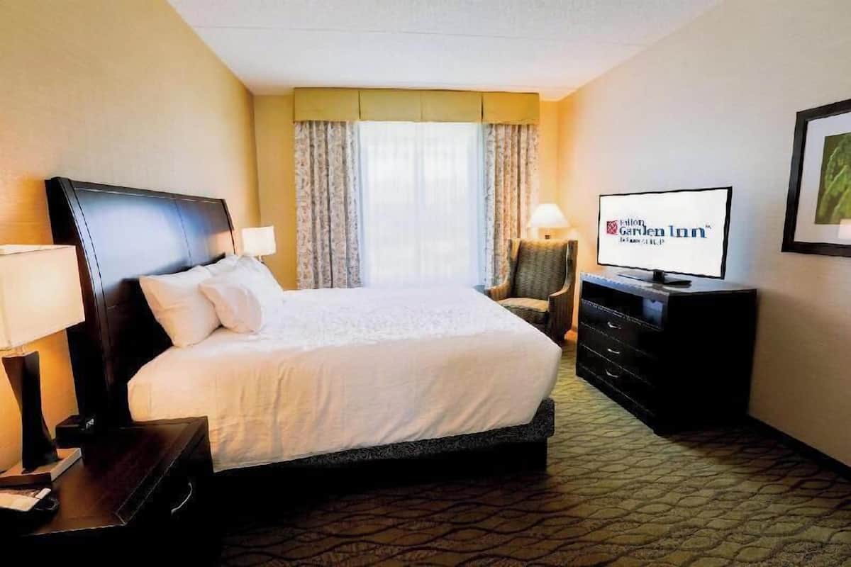 A hotel room with a bed, a television, a dresser, and a window with curtains.