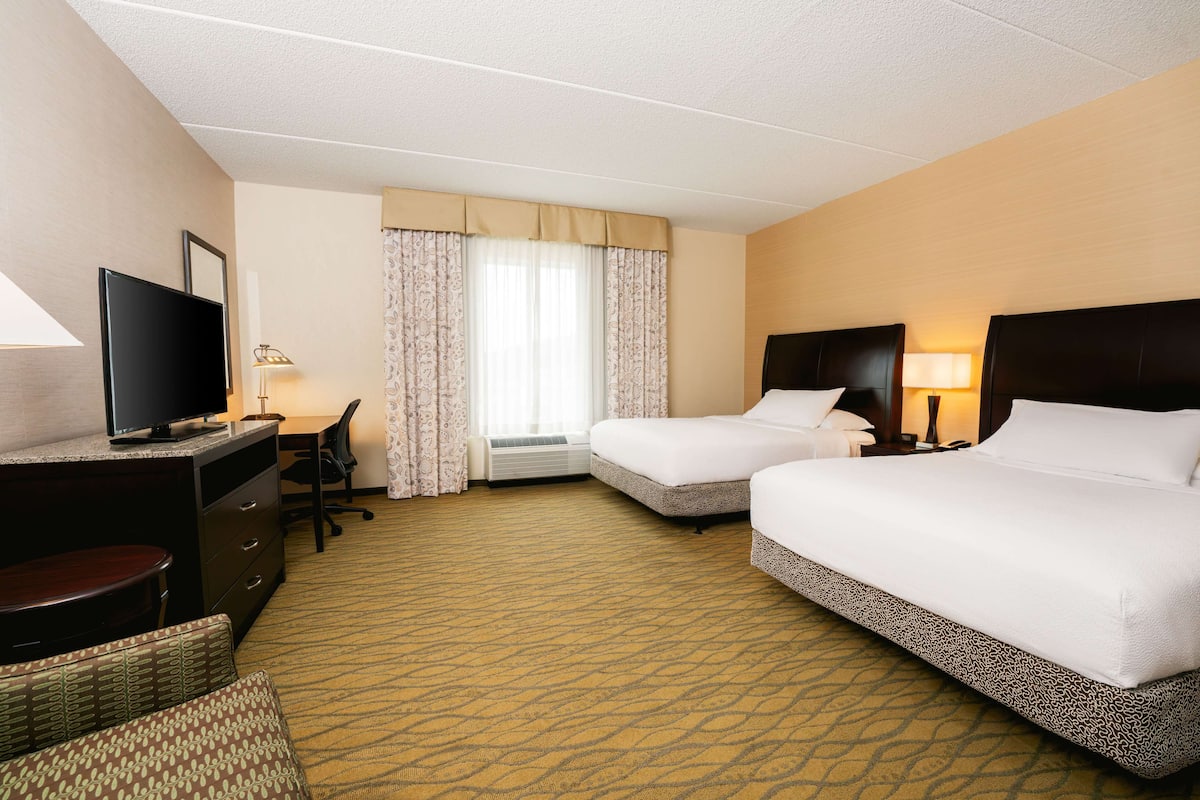A hotel room with two beds, a desk, a television, and a window with curtains.