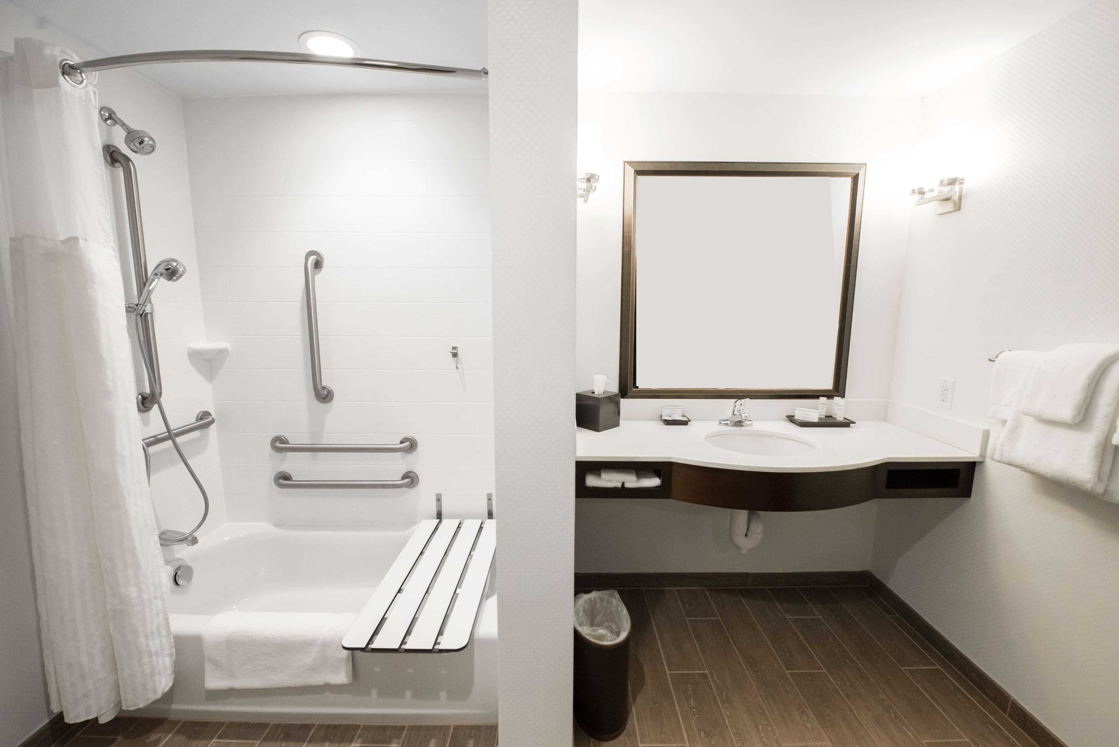 Een moderne badkamer met een inloopdouche, handgrepen, een bad, een wastafel en een spiegel.