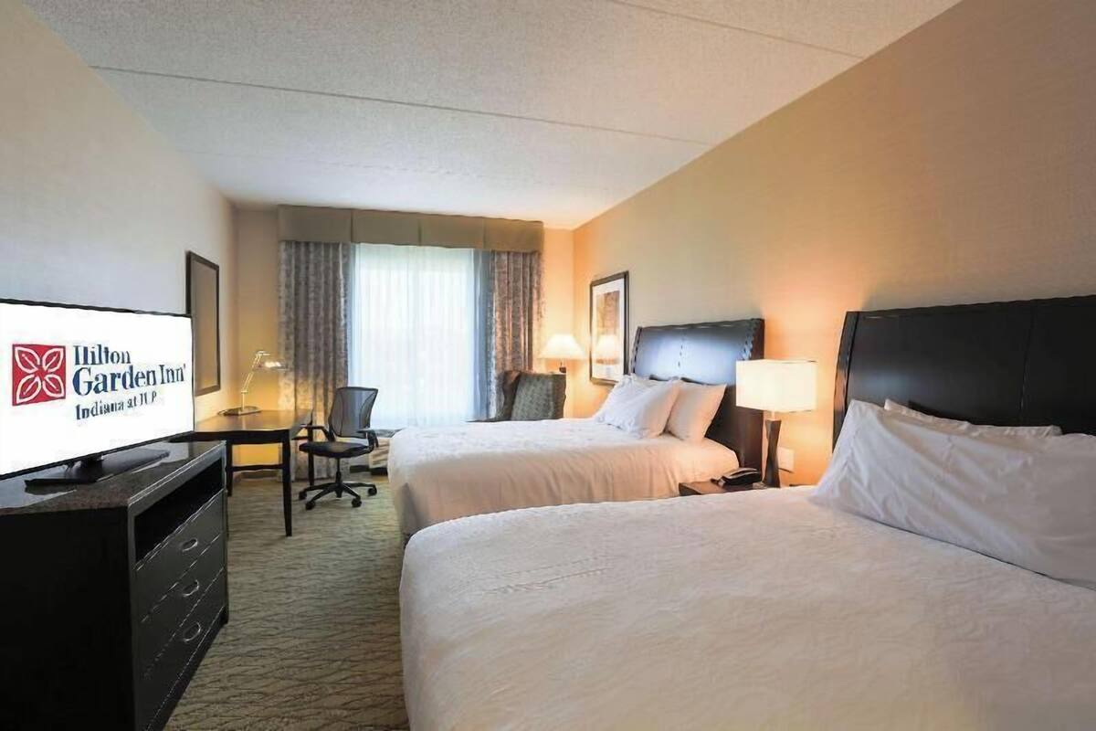 A hotel room with two beds, a desk, a television, and a chair.