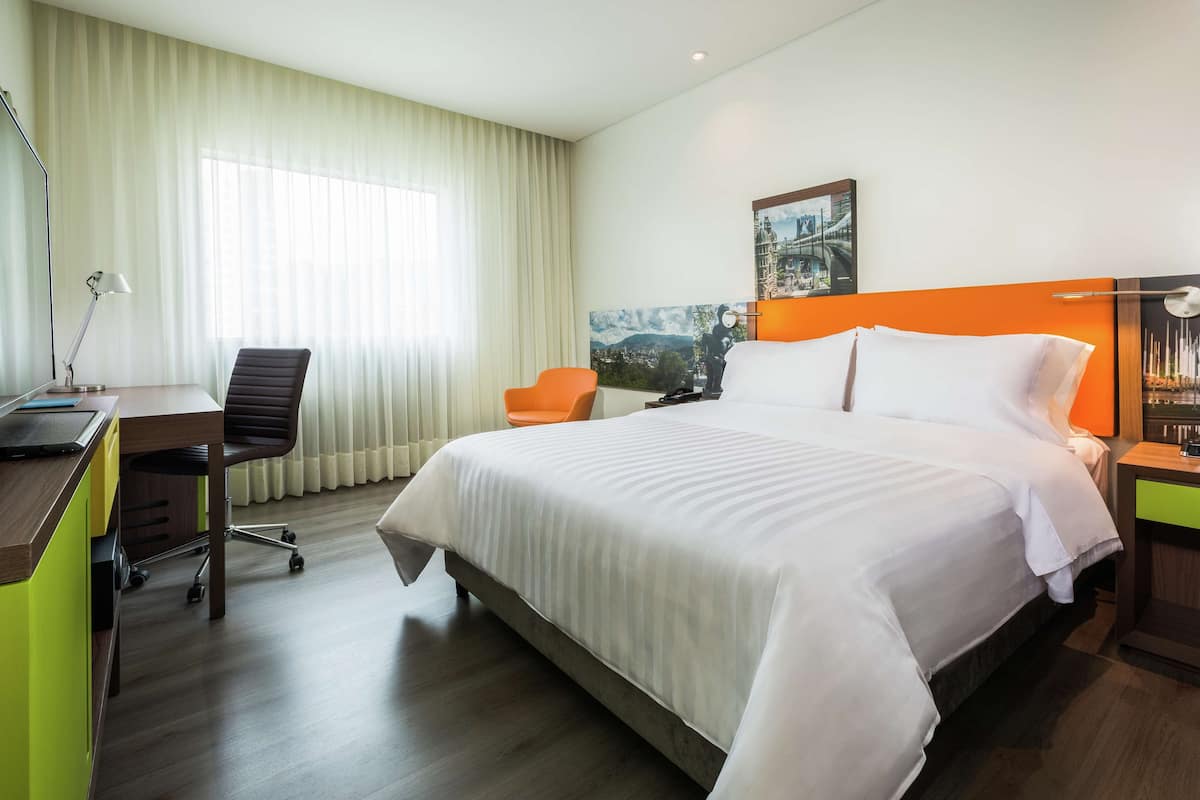 Une chambre d’hôtel avec un grand lit, un bureau avec une chaise, une lampe et un tableau au mur.