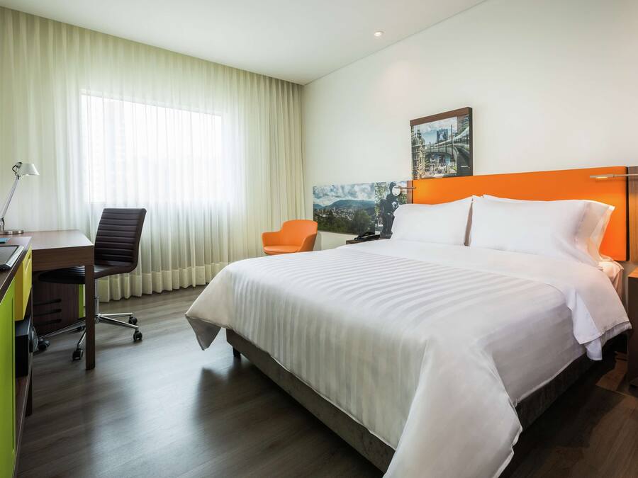 Une chambre d’hôtel avec un grand lit, un bureau avec une chaise, une lampe et un tableau au mur.