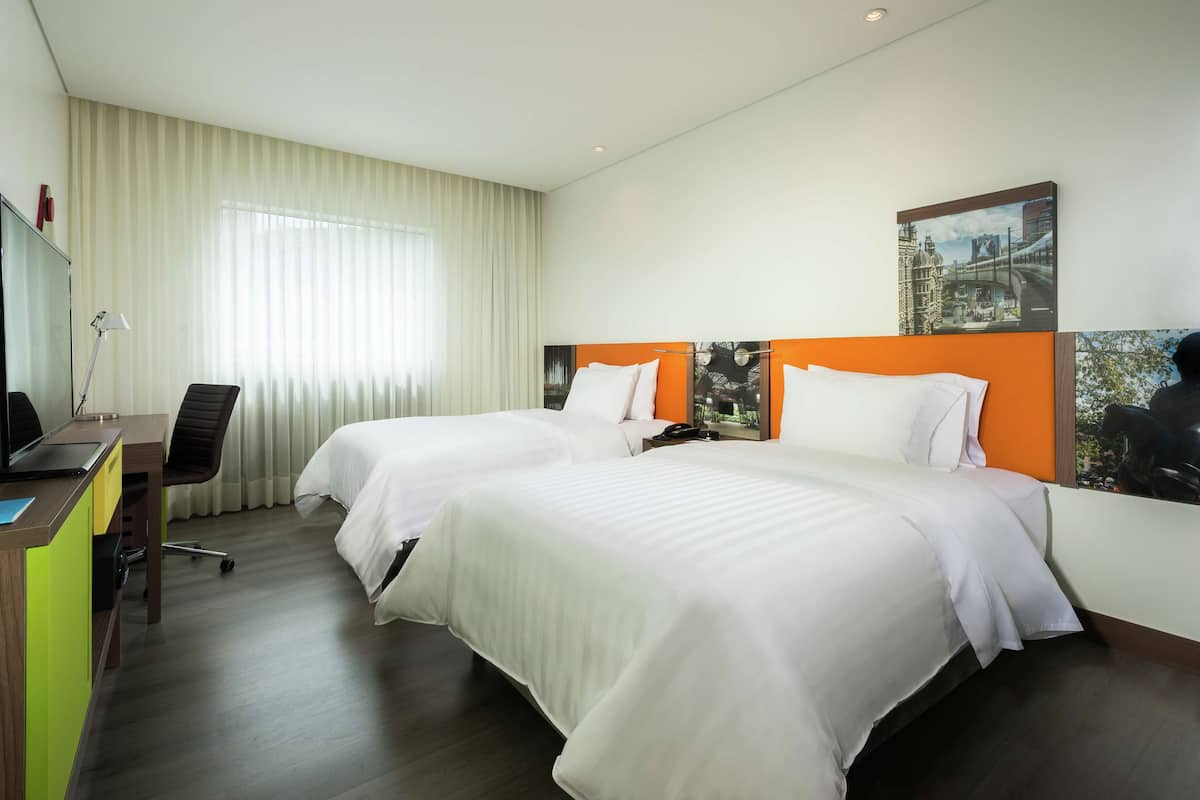Une chambre d’hôtel avec deux lits, un bureau avec un ordinateur, une chaise et une grande fenêtre avec des rideaux.