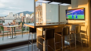 Zona de bar moderna con una gran pantalla de televisión, taburetes de bar y vistas a la ciudad.