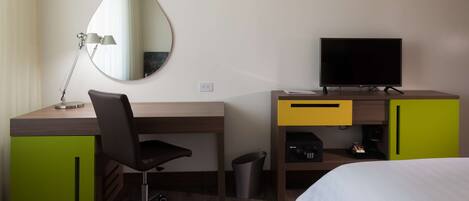 Una habitación de hotel con un escritorio de madera, una silla, un televisor, una cama y un espejo.
