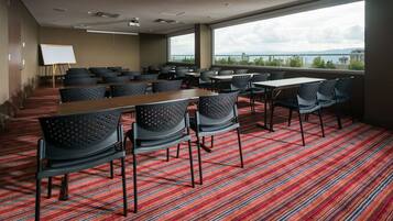 A conference room with a large window, a whiteboard, and multiple tables and chairs.