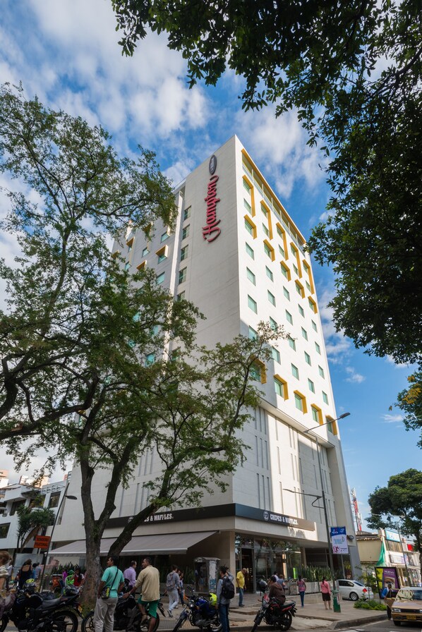 Un hotel de varios pisos con un llamativo letrero rojo en la fachada, un restaurante en la planta baja llamado "Chees & Waffles", y una entrada visible.