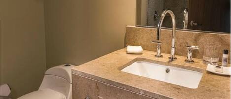 Un baño con inodoro blanco, lavamanos color beige con espejo arriba y una toalla en la encimera.