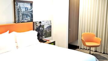 Ein Hotelzimmer mit einem Bett, einem Nachttisch, einem Sessel und zwei gerahmten Bildern an der Wand.