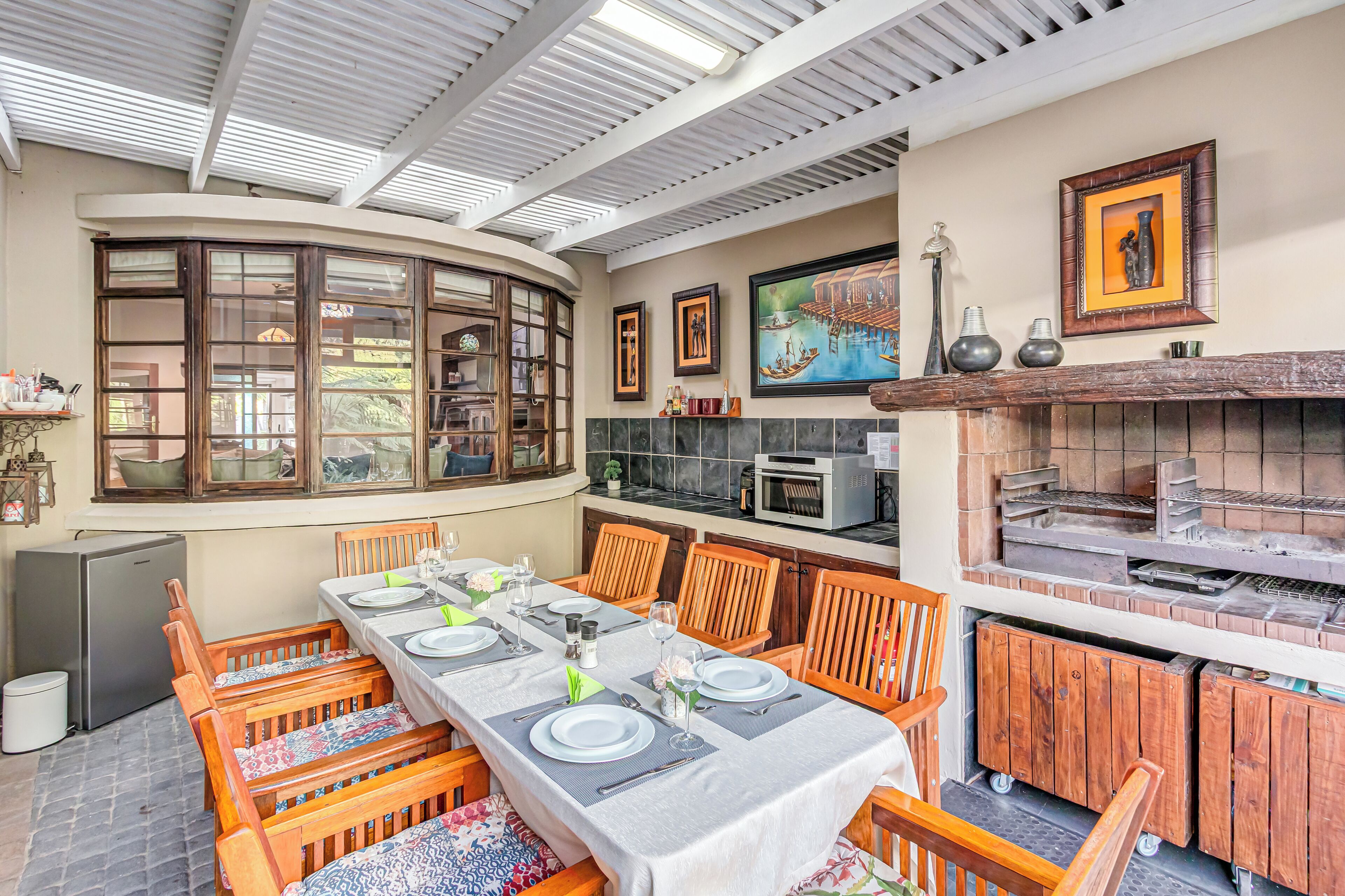 A dining area with a long table set for four, surrounded by wooden chairs, a built-in oven, and a microwave above the counter.