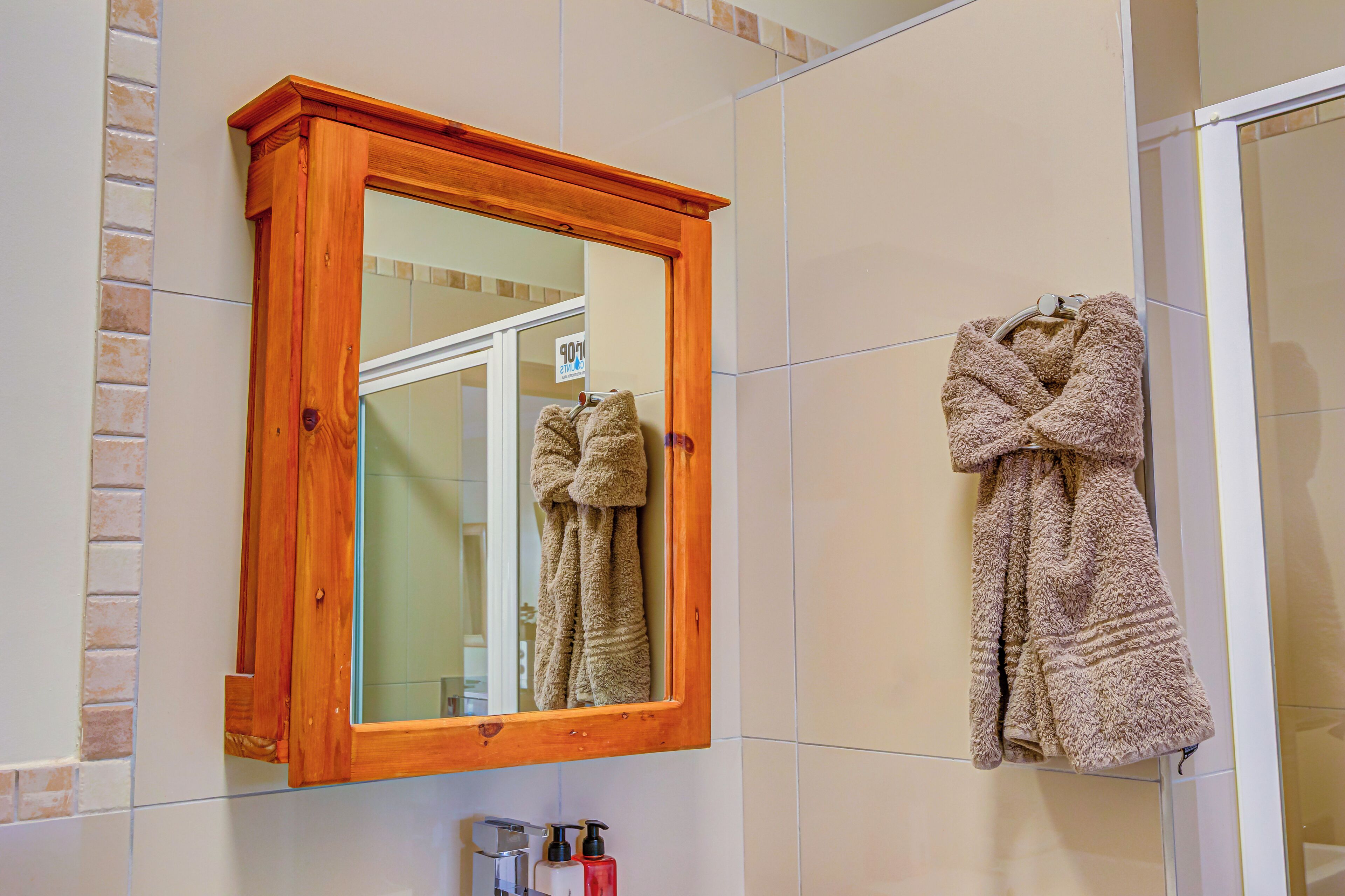 A bathroom with a wooden-framed mirror, a towel rack with a towel, and toiletries on the counter.