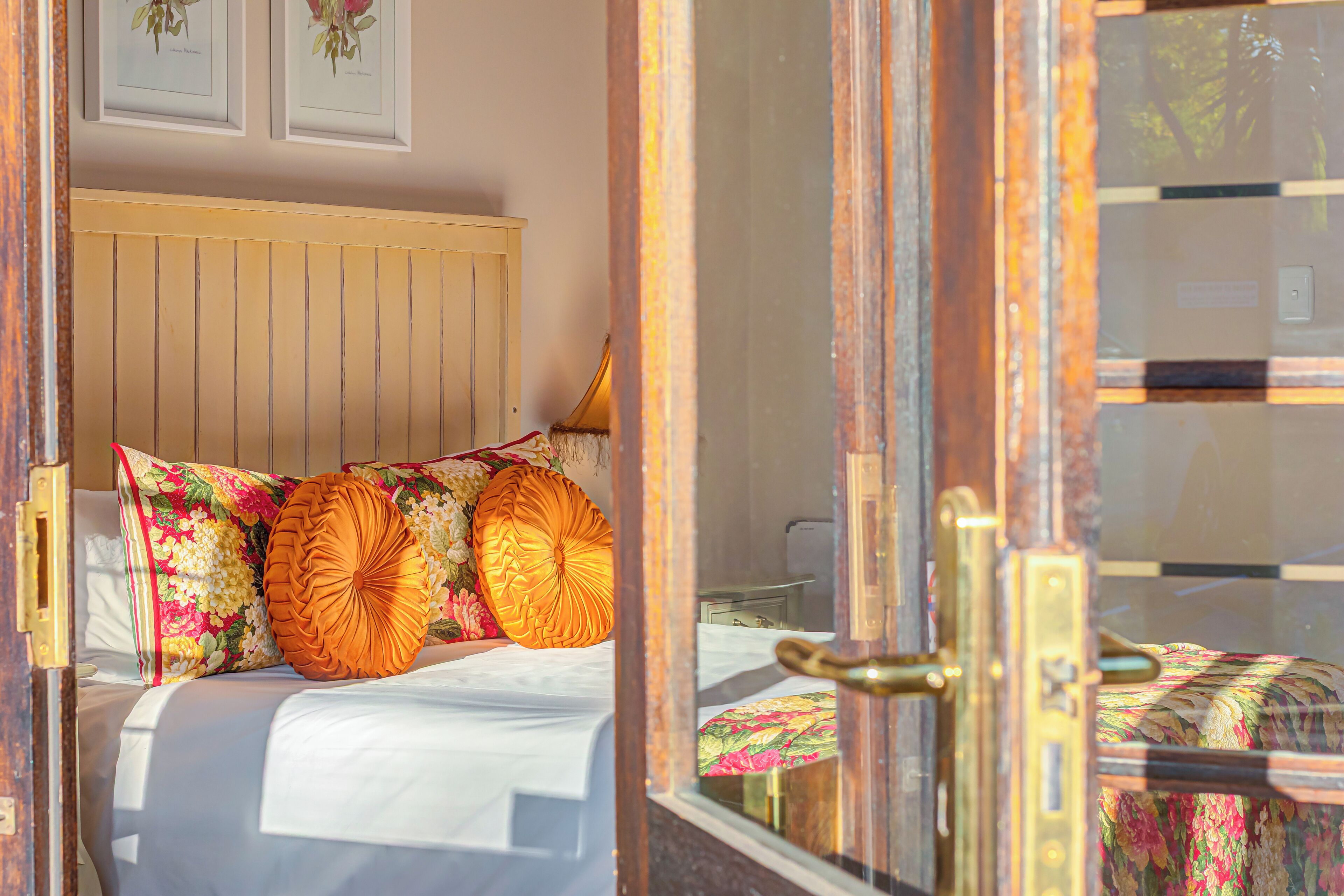 Ein Schlafzimmer mit einem Holzkopfteil, floralem Bettbezug und einer sichtbaren Tür mit Messinggriffen.