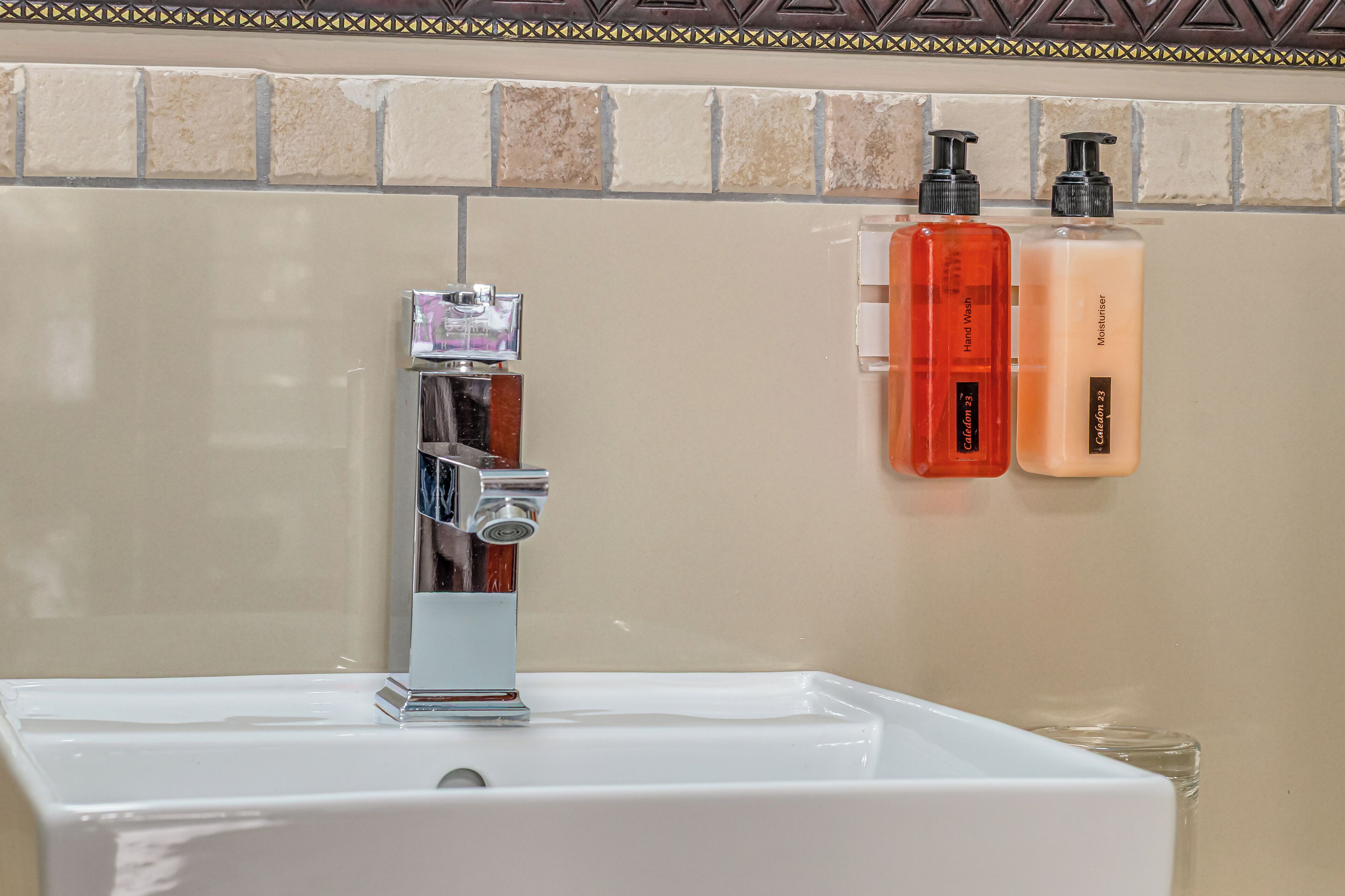 A bathroom with a white sink, a chrome faucet, and two hand soap dispensers on the wall.